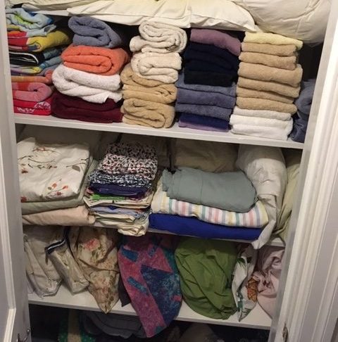 An organized linen closet of towels, sets of sheets folded and stored on three shelves