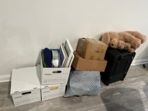 three banker boxes plus two smaller boxes on top of a bag and a large stuffed dog on top of a suitcase