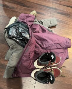 two winter coats thrown on floor with a pair of boots on top. 